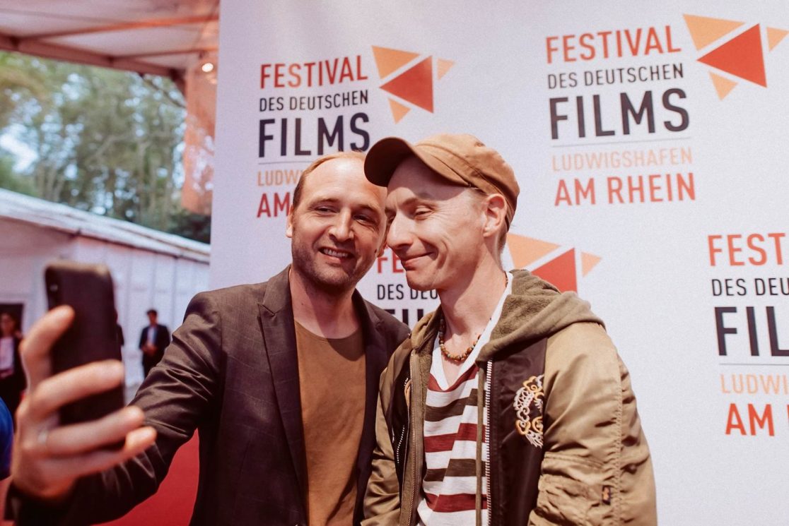 Zwei Besucher machen ein Selfie vor der Festivalwand des Festival des Deutschen Films Ludwigshafen