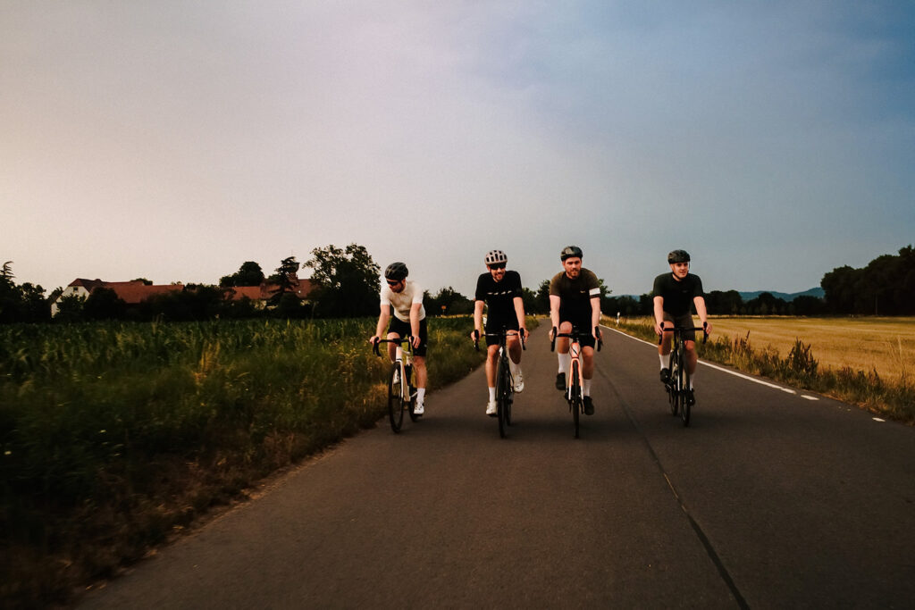 Vier Radfahrer nebeneinander auf einer flachen Landstraße im Abendlicht, Rennradfotografie von Sebastian Weindel