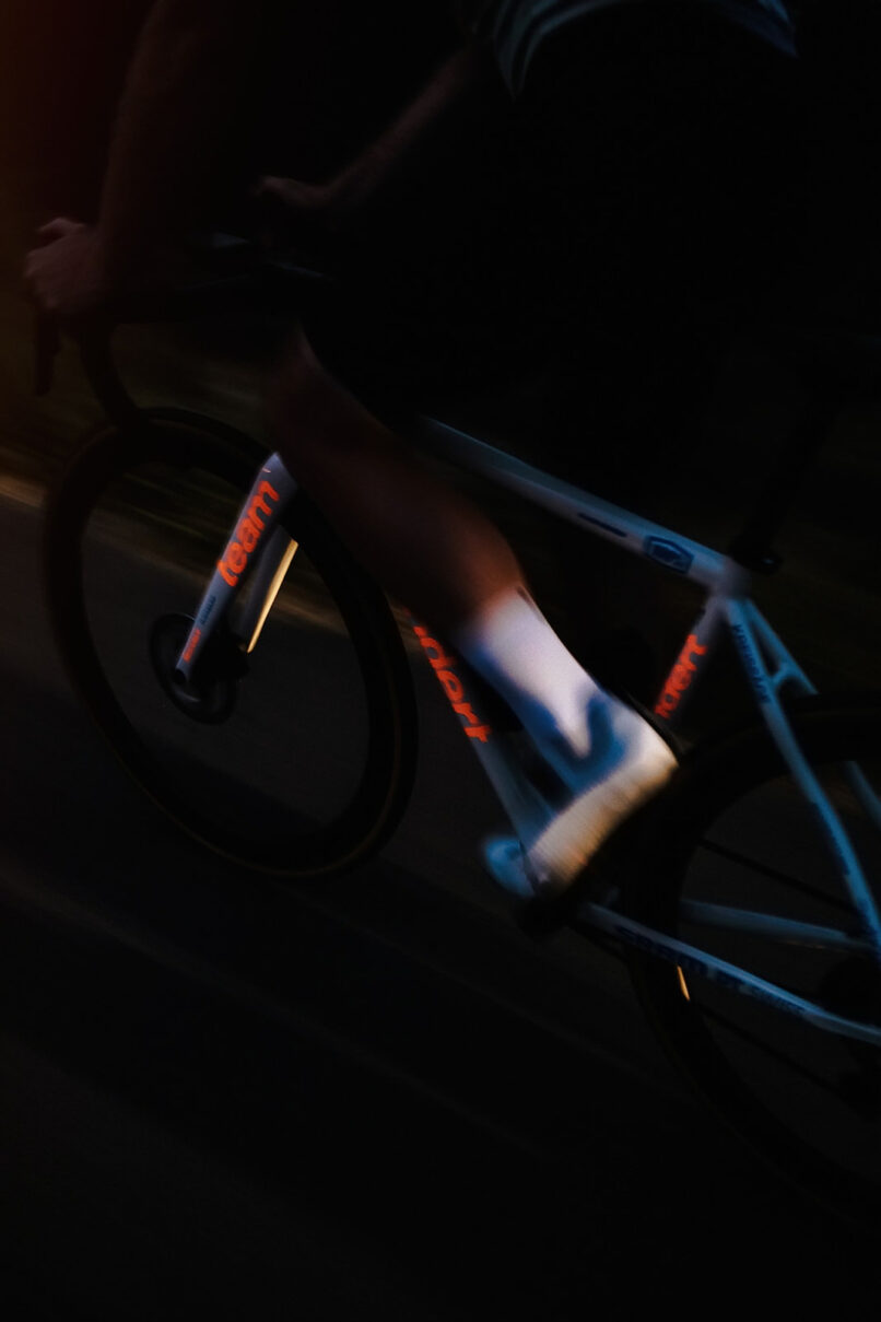 Radfahrer im Dunkeln, nur Rahmen und Beine angeleuchtet, starke Bewegungsunschärfe, Rennradfotografie von Sebastian Weindel