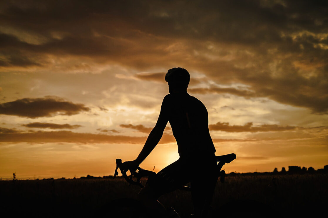 Silhouette eines Radfahrers mit Helm vor goldenem Abendhimmel, Rennradfotografie von Sebastian Weindel